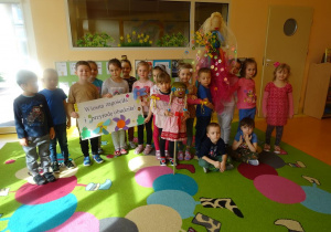 Grupa dzieci prezentuje plakat, panią Wiosnę i kukłę Marzanny.